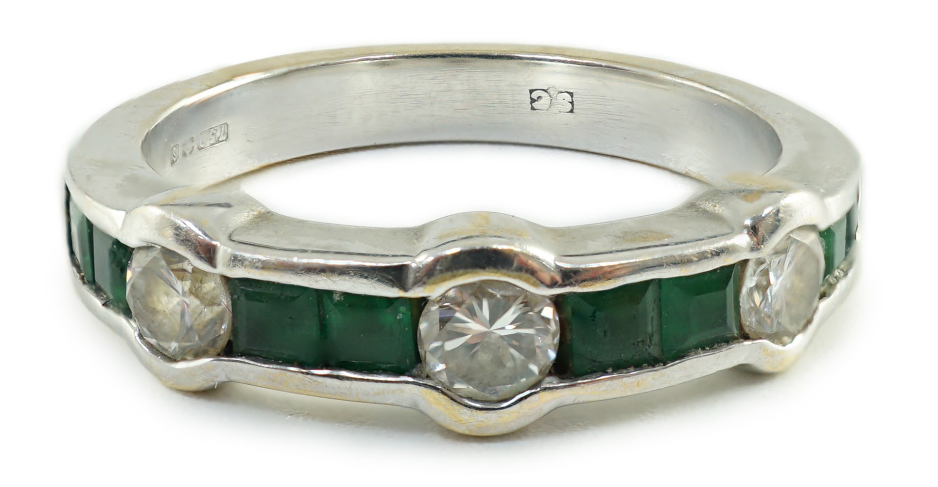 A modern 18ct white gold, three stone collet set diamond and eight stone channel set emerald half hoop ring